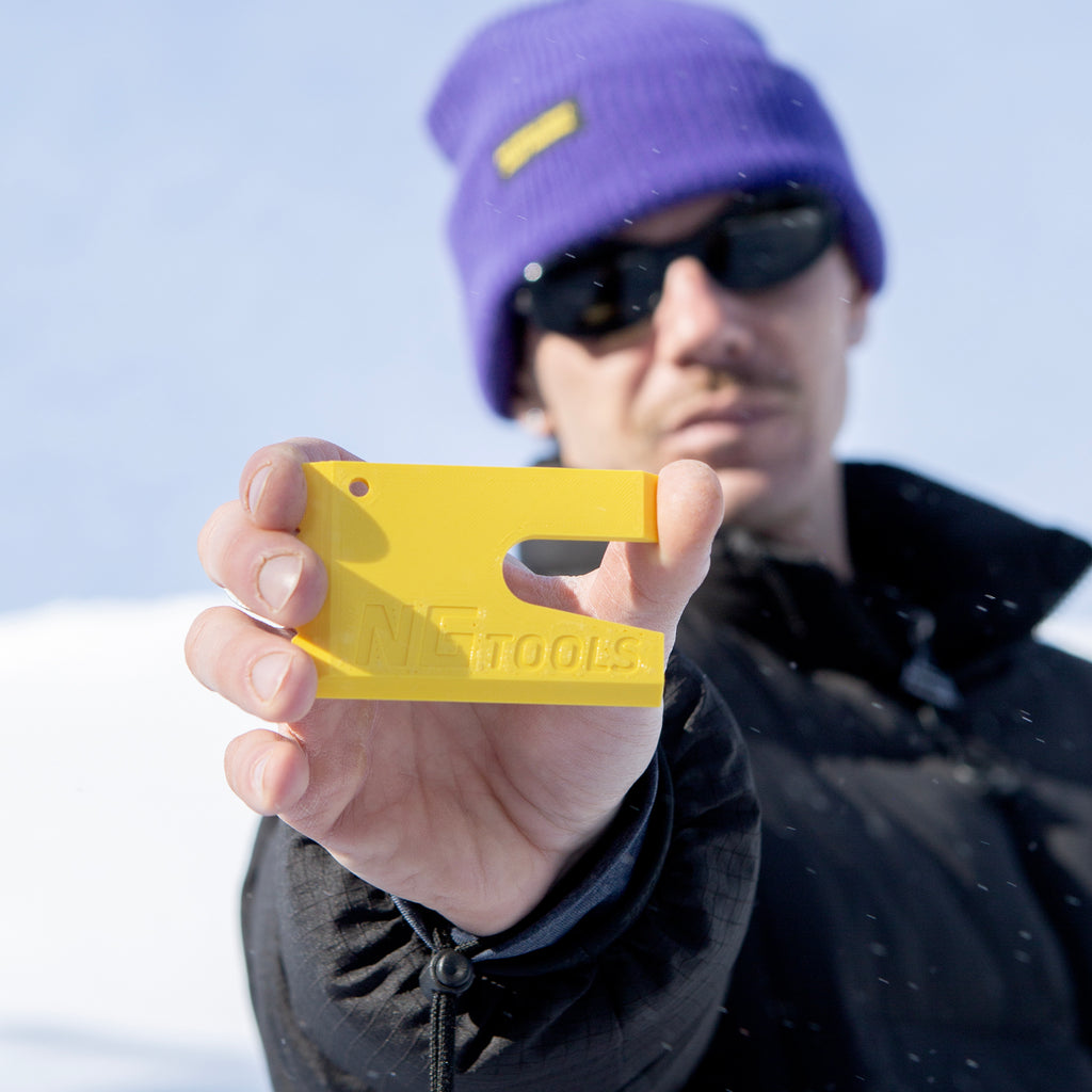 NGTOOLS Small Snowboard Binding Multitool in yellow on snow, used by a model. Compact, durable, and perfect for snowboarders, shapers, skialping, and splitboarding. Ideal for quick binding adjustments and gear maintenance.