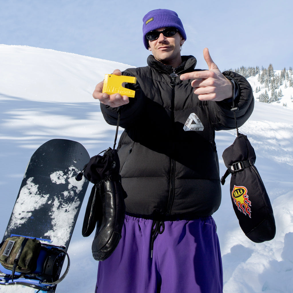 NGTOOLS Small Snowboard Binding Multitool in yellow on snow, next to a camo NGTOOLS Snowboard Binding Bag – High-Back Backpack. Compact, durable, and ideal for snowboarders, shapers, skialping, and splitboarding.