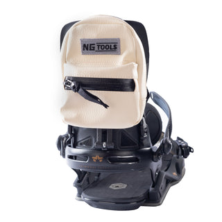 NG Snowboard Binding Bag in off-white leather, securely attached to a snowboard binding. High-back snowboard backpack for carrying tools, wax, or essentials while riding.