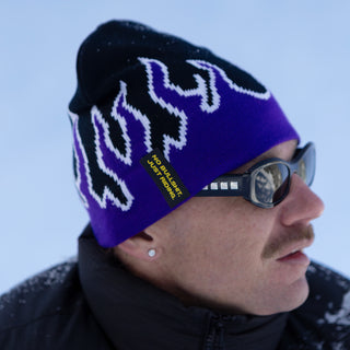 NG Graphic Beanie – purple fire design on snow, worn by a model at Absolut Park. Features bold graphics and ‘No Bullshit, Just Riding’ label. 100% acrylic, warm, and durable for snowboarding, skiing, and winter wear.