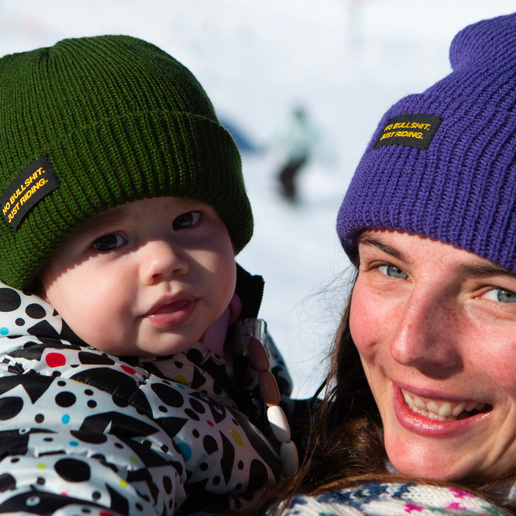 Shop our Kids Classic Beanie—small fit, 100% acrylic, perfect for kids who love snowboarding, skiing, and staying warm. Featuring the "No bullshit, just riding" label, this beanie combines style and warmth for all winter adventures. Ideal winter gear for young shredders! Kids Model. Green Color. Purple Beanie. 